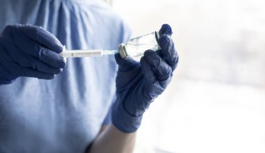 Mavi eldivenli kadın eller bir şırınga ve bir şişe ilaç ya da aşı taşıyor.