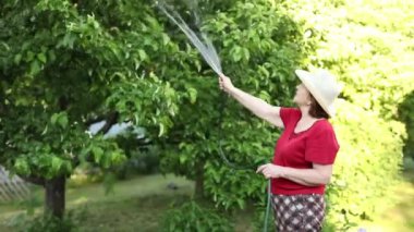Bahçesindeki yaşlı bir kadın, ağaçları hortumla sular..
