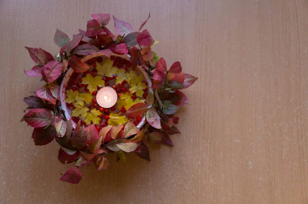 Ahşap bir yüzey üzerinde yapraklar ve dağ küllerinden oluşan bir mumla sonbahar tesisi.