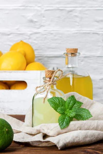 Lemon and lime syrups in glass bottle and fruits in the crate on the background. Side view of fresh citrus.