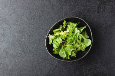 Green salad leaves in bowl on black table with copy space. Fresh and healthy food. Top view.