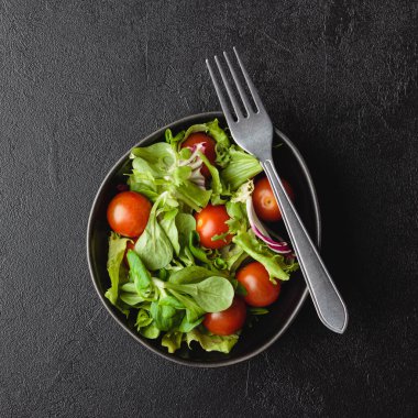 Yeşil salata yaprakları ve siyah masada kiraz domatesleri. Taze ve sağlıklı yiyecekler. Üst görünüm.