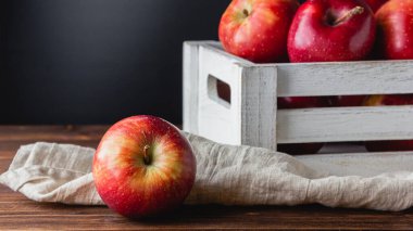 Tahta bir masanın üzerindeki sandıkta kırmızı elmalar. Taze meyvelerin yan görünümü.
