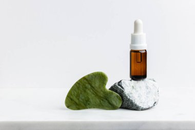 Yeşil yeşillik gua sha masaj aleti ve beyaz mermerin üzerinde yüz için serum. Moda bir kozmetik alet. Yaşlanma karşıtı terapi. Yan görüş. Düz yatıyordu. Boşluğu kopyala.