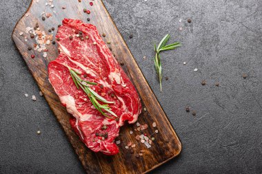 Tahta kesme tahtasında çiğ et. Büyük bir parça pişmemiş kırmızı et ve arka planda biberiye ve fotokopi alanı var..