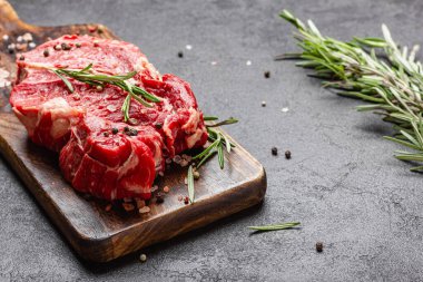 Tahta kesme tahtasının üzerinde pişmemiş büyük bir parça kırmızı et. Koyu arkaplanda biberiyeli çiğ et..