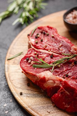 Büyük bir parça pişmemiş kırmızı et ve koyu arkaplanda biberiye. Tahta tepside çiğ et.