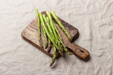Keten masa örtüsünün üzerindeki tahta kesme tahtasındaki yeşil kuşkonmaz. Taze ve doğal pişmemiş kuşkonmaz. Sağlıklı bitki yiyeceği.