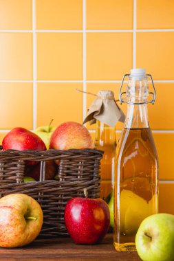 Ahşap bir masada şişede elma şarabı. Elmalar sepette. Taze meyvelerin yan görünümü.