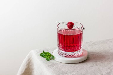 Ahududu bardakta, misketin üstünde hafif arkaplanlı naneli kokteyl. Yaz kırmızı içeceği.