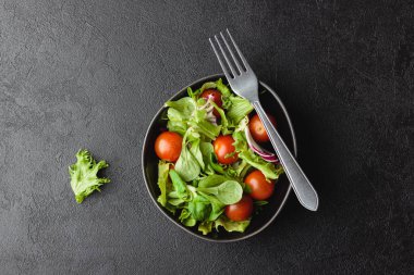 Yeşil salata yaprakları ve siyah masada kiraz domatesleri. Taze ve sağlıklı yiyecekler. Üst görünüm.