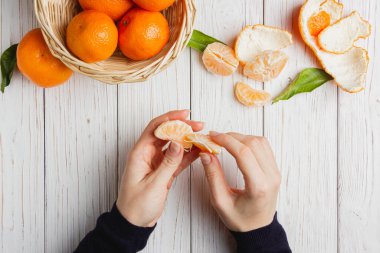 Saman sepetinde mandalinalar ve beyaz ahşap bir masada kadın elleri. Taze mandalinaların üst görüntüsü.