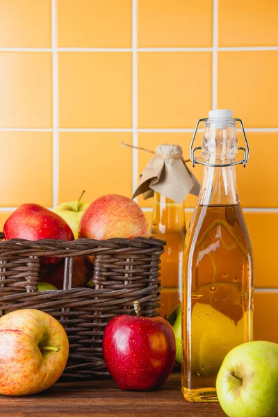 Ahşap bir masada şişede elma şarabı. Elmalar sepette. Taze meyvelerin yan görünümü.