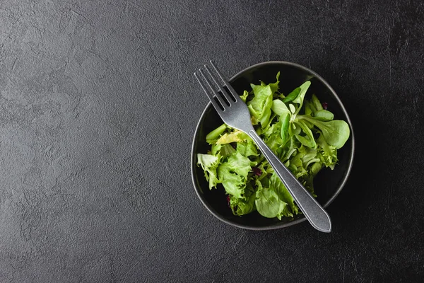 Green salad leaves in bowl on black table with copy space. Fresh and healthy food. Top view.