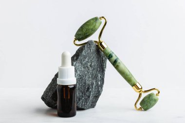 Beyaz mermer üzerinde yüz için yeşil yeşim taşlı masaj aleti olan serum. Moda bir kozmetik alet. Yaşlanma karşıtı terapi. Yan görüş. Düz yatıyordu. Boşluğu kopyala.