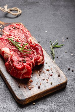 Tahta kesme tahtasında çiğ et. Büyük bir parça pişmemiş kırmızı et ve koyu arkaplanda biberiye..