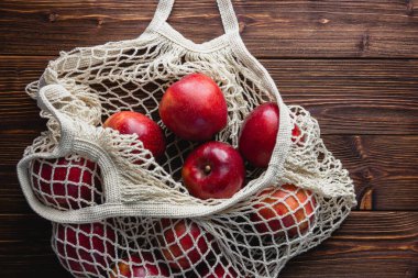 Ahşap bir arka planda şebeke çantasındaki kırmızı elmalar. Kopya alanı olan taze meyvelerin üst görünümü.