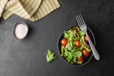 Yeşil salata yaprakları ve siyah masada kiraz domatesleri. Taze ve sağlıklı yiyecekler. Üst görünüm.