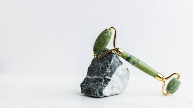 Beyaz mermer üzerinde yüz için yeşil taşlı masaj aleti. Moda bir kozmetik alet. Yaşlanma karşıtı terapi. Yan görüş. Düz yatıyordu. Boşluğu kopyala.