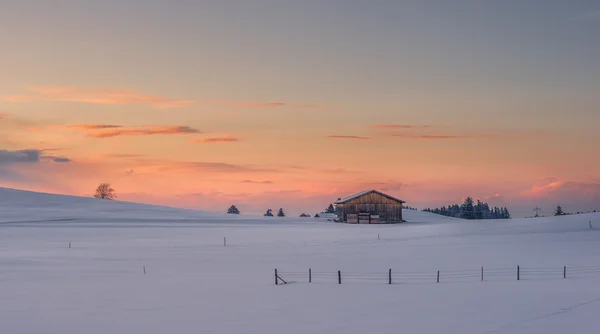 Simple cabane au coucher du soleil en hiver dans un pré enneigé et un ciel lumineux — Photo