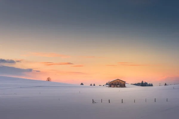 Egy kunyhó a lemenő nap utolsó sugarai napnyugtakor ég télen — Stock Fotó