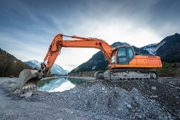 Sidovy av orange spade grävare på grus på sjön och blue sky — Stockfoto