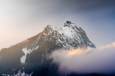 Renkli bulutlar kışın gün batımında Gehrenspitz dağının zirvesinden geçer.