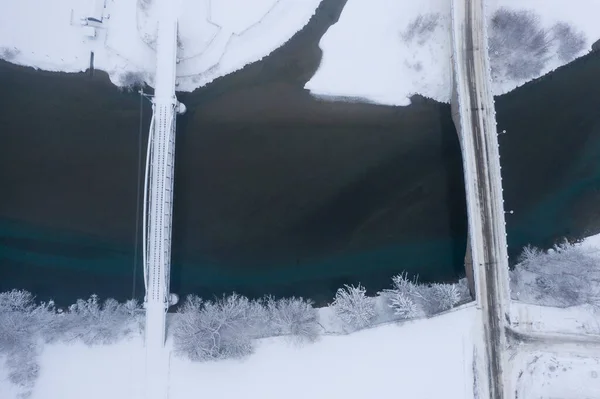 Bird\'s eye view of a car and a railroad bridge over the river Lech from above in the white snowy winter