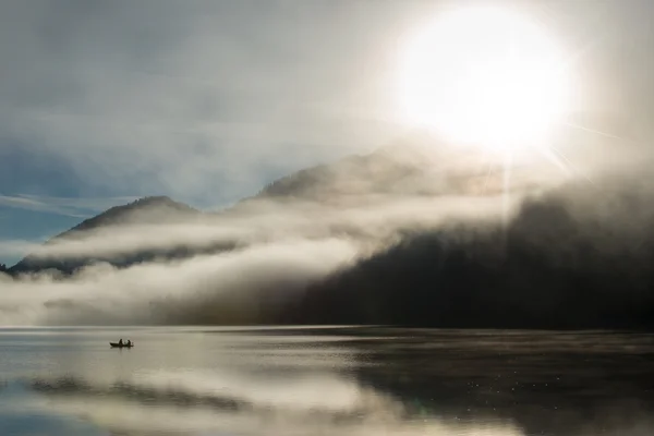 Sonnenaufgang am österreichischen See mit Fischerboot mit Staub und Nebel in den Alpen — Stockfoto