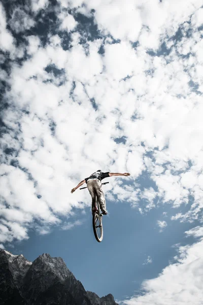 Stunt motociclista sporco con le mani libere in alto nel cielo nuvoloso e montagne — Foto Stock