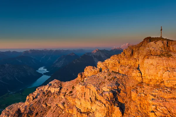 Laranja rochas brilhantes de pico de montanha com cruz ao pôr do sol — Fotografia de Stock
