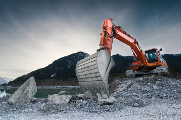 Zware oranje graafmachine met schop staande op heuvel met rotsen — Stockfoto