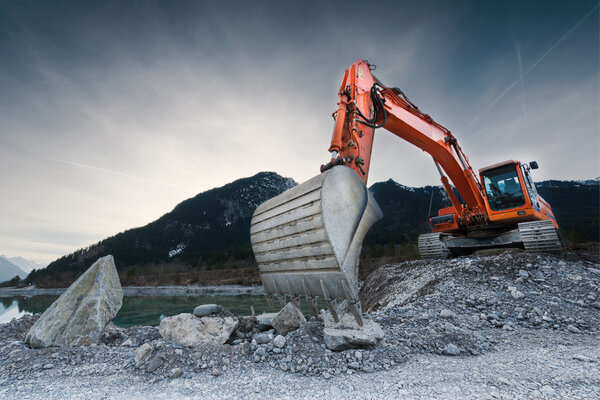 Heavy organge excavator with shovel standing on hill with rocks