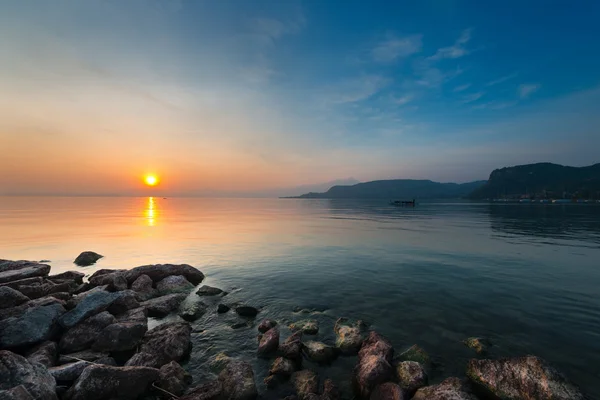 Moody puesta de sol en el lago gardasee con rocas en la costa — Foto de Stock