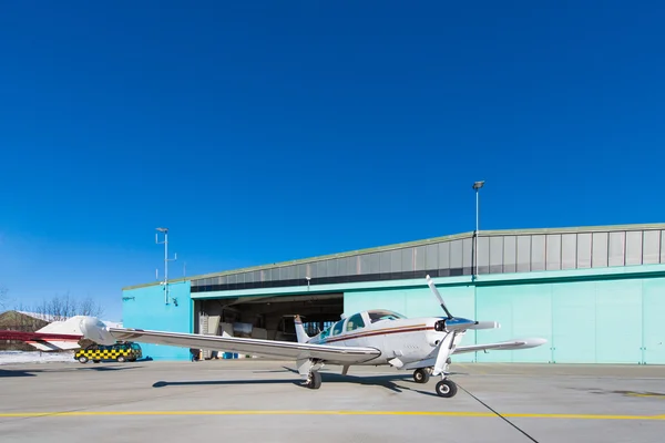 Pequeno avião em pé diante do hangar da aeronave no céu azul — Fotografia de Stock