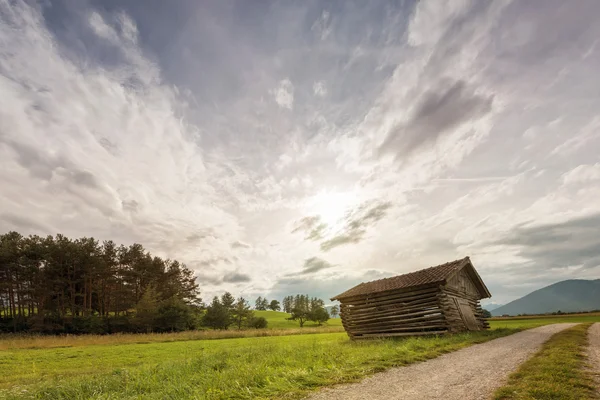 Antiguo cobertizo de madera oblicuo en el prado al atardecer — Foto de Stock