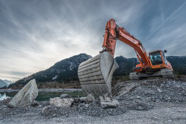 Büyük bir kürekle çakıl yığınında büyük bir turuncu kazıcı.