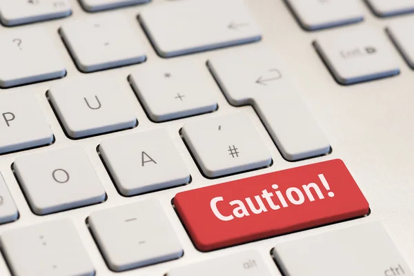 Computer keyboard with the word caution on red key — Stock Photo, Image