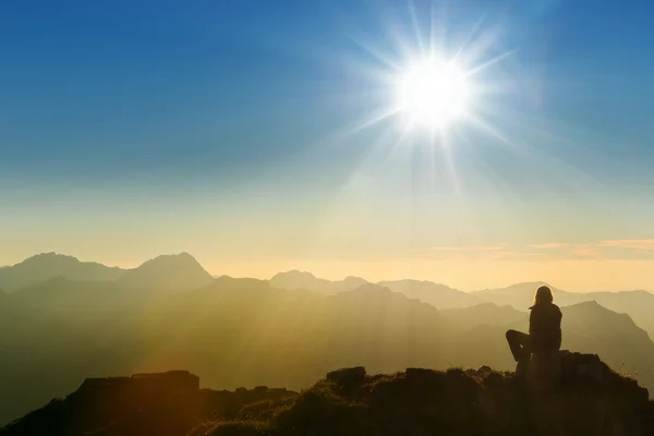 Solitaria persona triste sentada en la cumbre de la montaña al amanecer — Foto de Stock