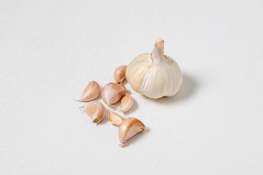 Beyaz bir masada bir tutam sarımsak. Etrafta ayrı ayrı sarımsak karanfilleri var.