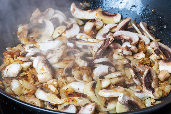 Sliced champignon mushroom is saute on onion in a pan