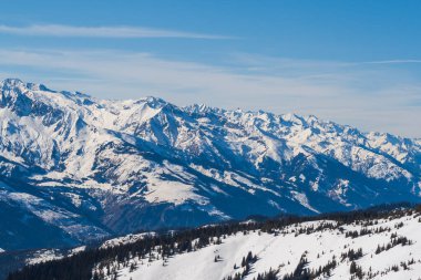 Avusturya 'nın Zell am bölgesindeki karlı dağ zirveleri. Arka planda dramatik bulutlarla dolu mavi bir gökyüzü var..