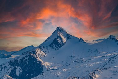 Avusturya 'nın Zell am bölgesindeki karlı dağ zirveleri. Arka planda dramatik bulutlarla dolu mavi bir gökyüzü var..