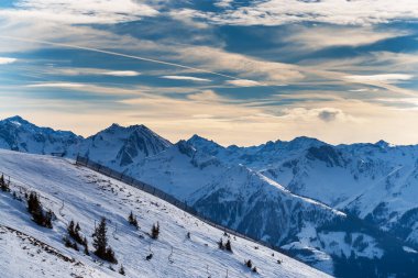 Avusturya 'nın Zell am bölgesindeki karlı dağ zirveleri. Arka planda dramatik bulutlarla dolu mavi bir gökyüzü var..