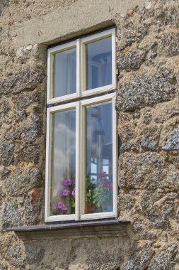 Eski ahşap pencere. Pencerenin etrafında taş bir duvar var. Pencerede bir çiçek var..