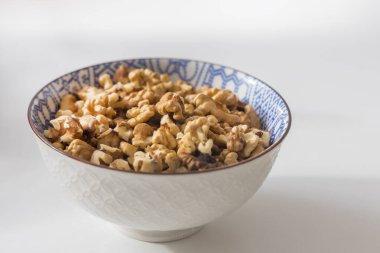 Kabuklu ceviz çekirdekleri ile dolu stüdyo tarzı detaylı bir fotoğraf. Besin zengini fındıklar, kendine özgü mavi ve beyaz geometrik desenli küçük beyaz bir kasenin içinde bulunur.