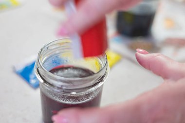 Parlak kırmızı Paskalya yumurtası boyasının döküldüğü ya da çözündüğü cam kavanozun yakın plan görüntüsü. Kavanozun dibindeki yoğunlaşmış renk suda çözünüyor.