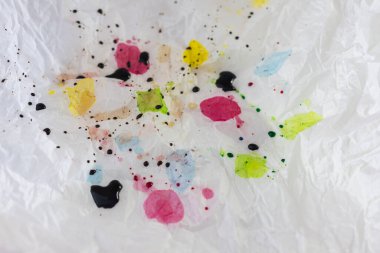 Parlak yumurta boyası damlaları, kırmızı, sarı, yeşil ve mavi, küçük koyu renk lekeleri ile kaplanmış, buruşuk beyaz kağıt veya plastik yüzey soyut yakın çekim.