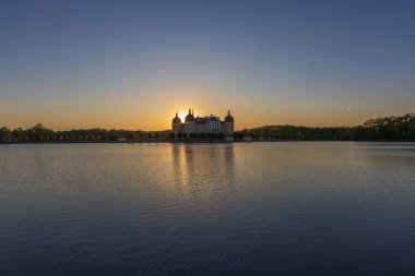 Gün batımında Moritzburg Kalesi 'nde, batan güneş binanın tam arkasında. Castle Pond 'un sakin yüzeyinde muhteşem bir yansıma..
