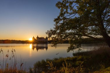 Moritzburg Kalesi 'nde romantik bir gün batımı. Barok adasının şatosu sakin su yüzeyine yansıyor. Batan güneş altın yansımalar yaratır..